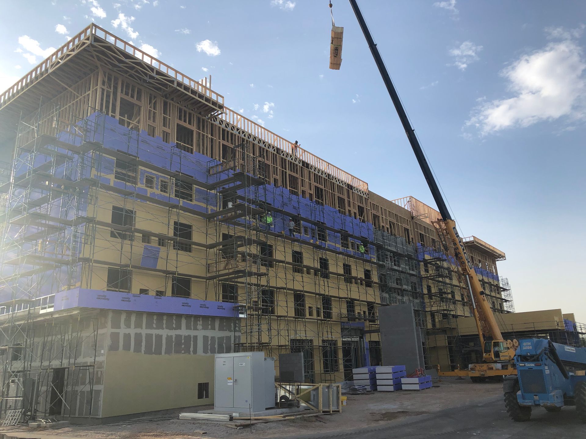Construction of a multi-story building, scaffolding, crane, blue protective wrap, clear sky.