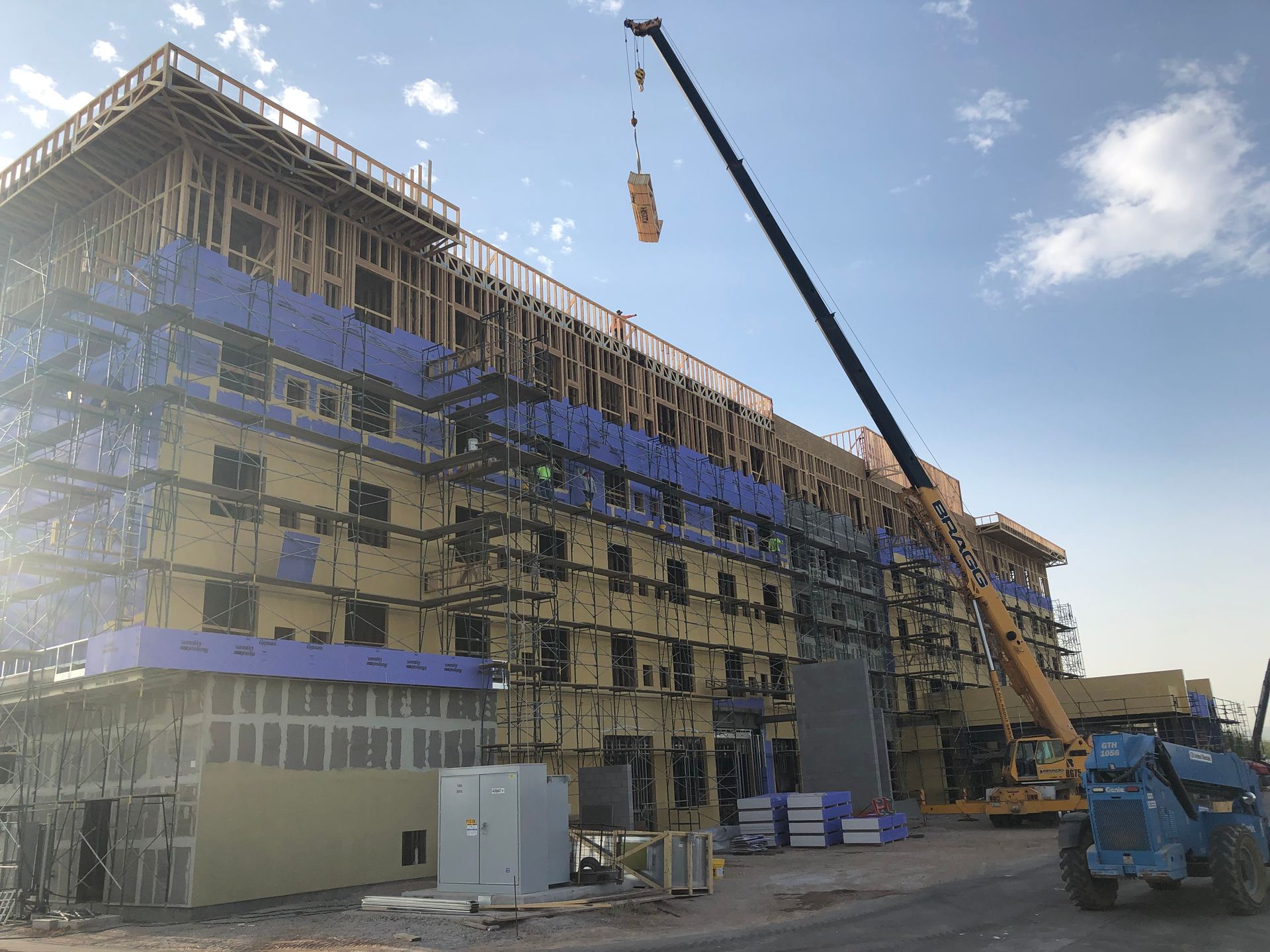 Building under construction with a crane lifting materials; scaffolding and wooden framing are visible.