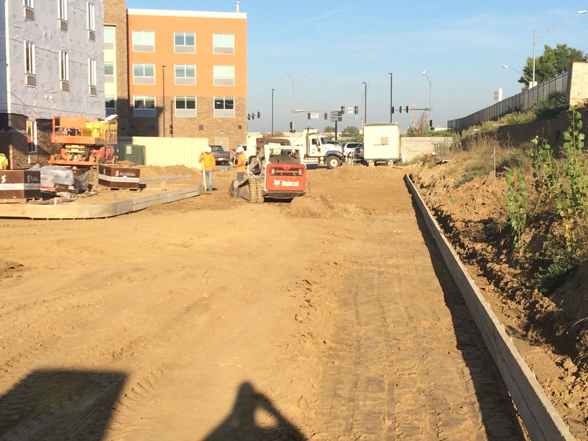 Construction site with a small excavator moving dirt; building in background.
