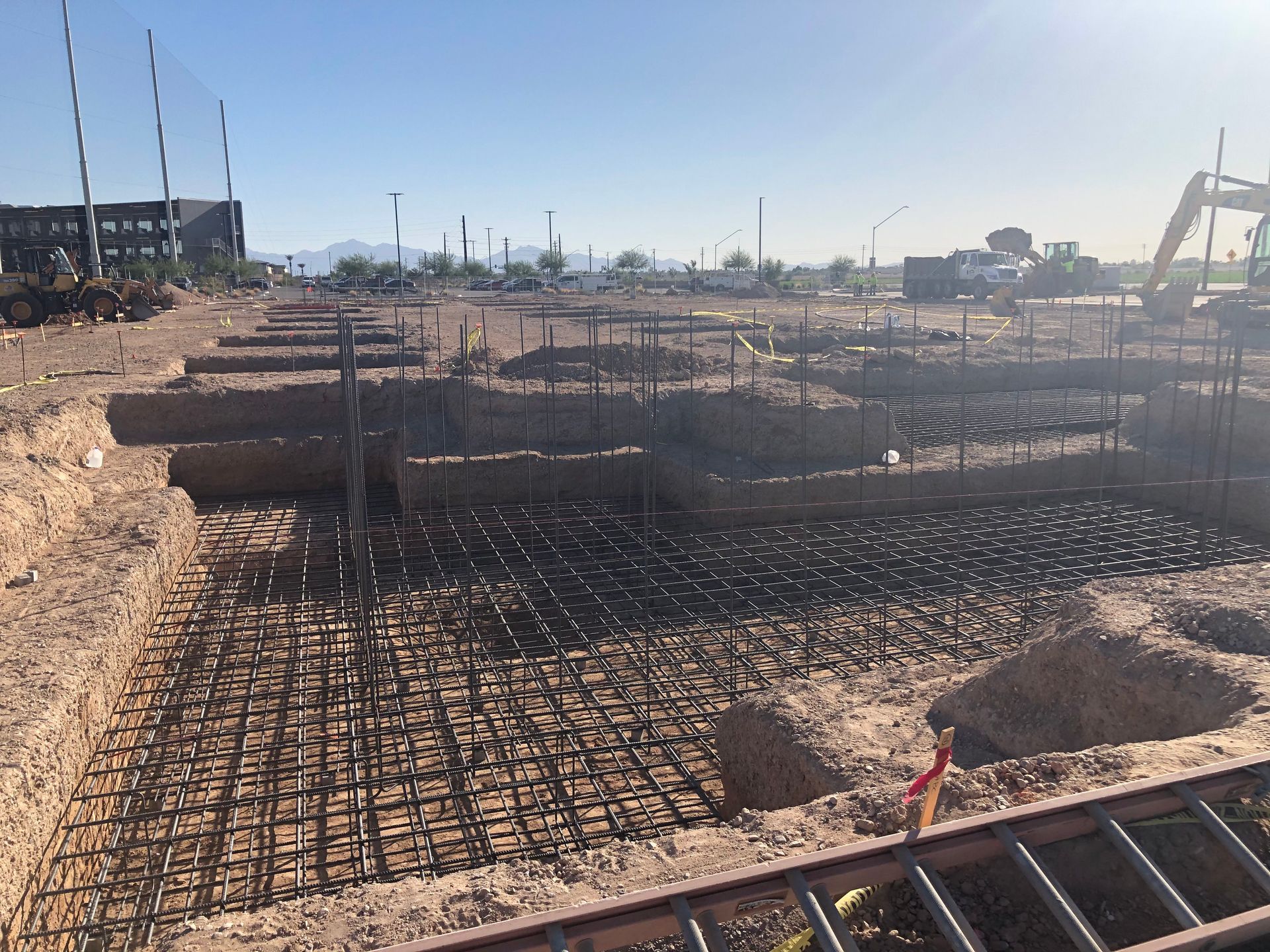 Construction site with exposed rebar, trenches, and earthworks under a clear sky.