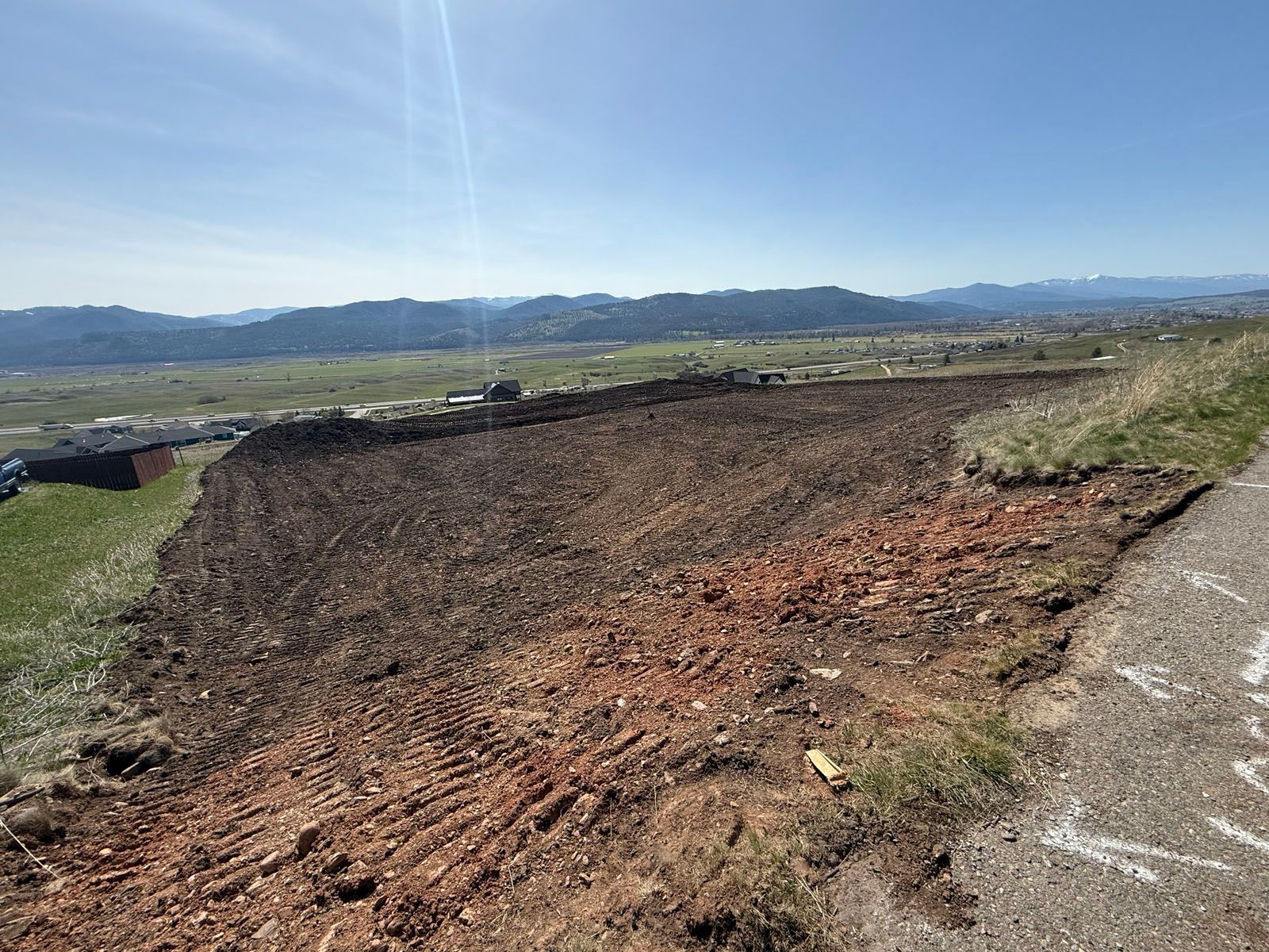View of a leveled dirt field, likely for construction, with distant hills and a clear blue sky.