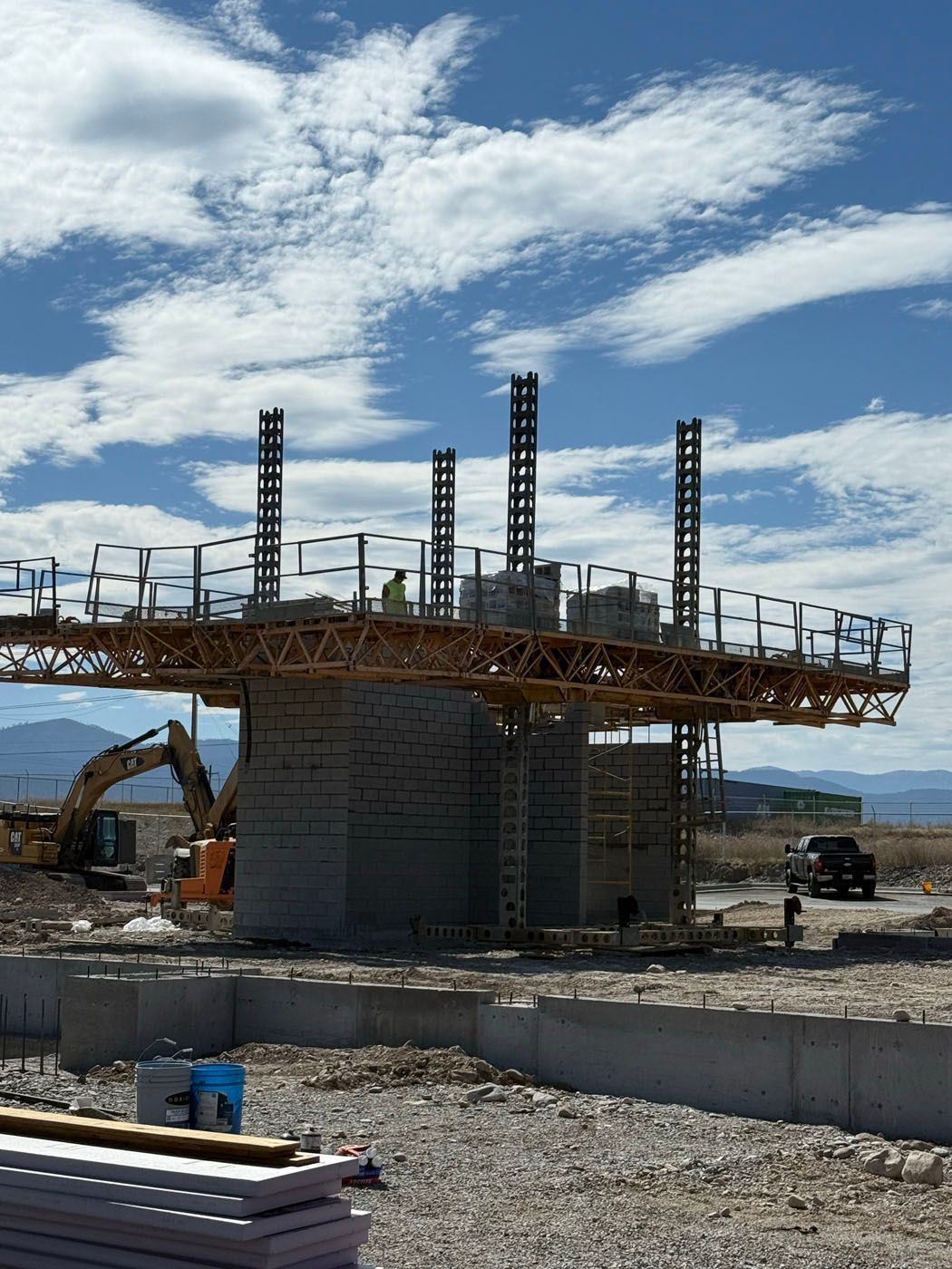 Construction site with concrete structures, workers, excavator, and a clear, blue sky with clouds.