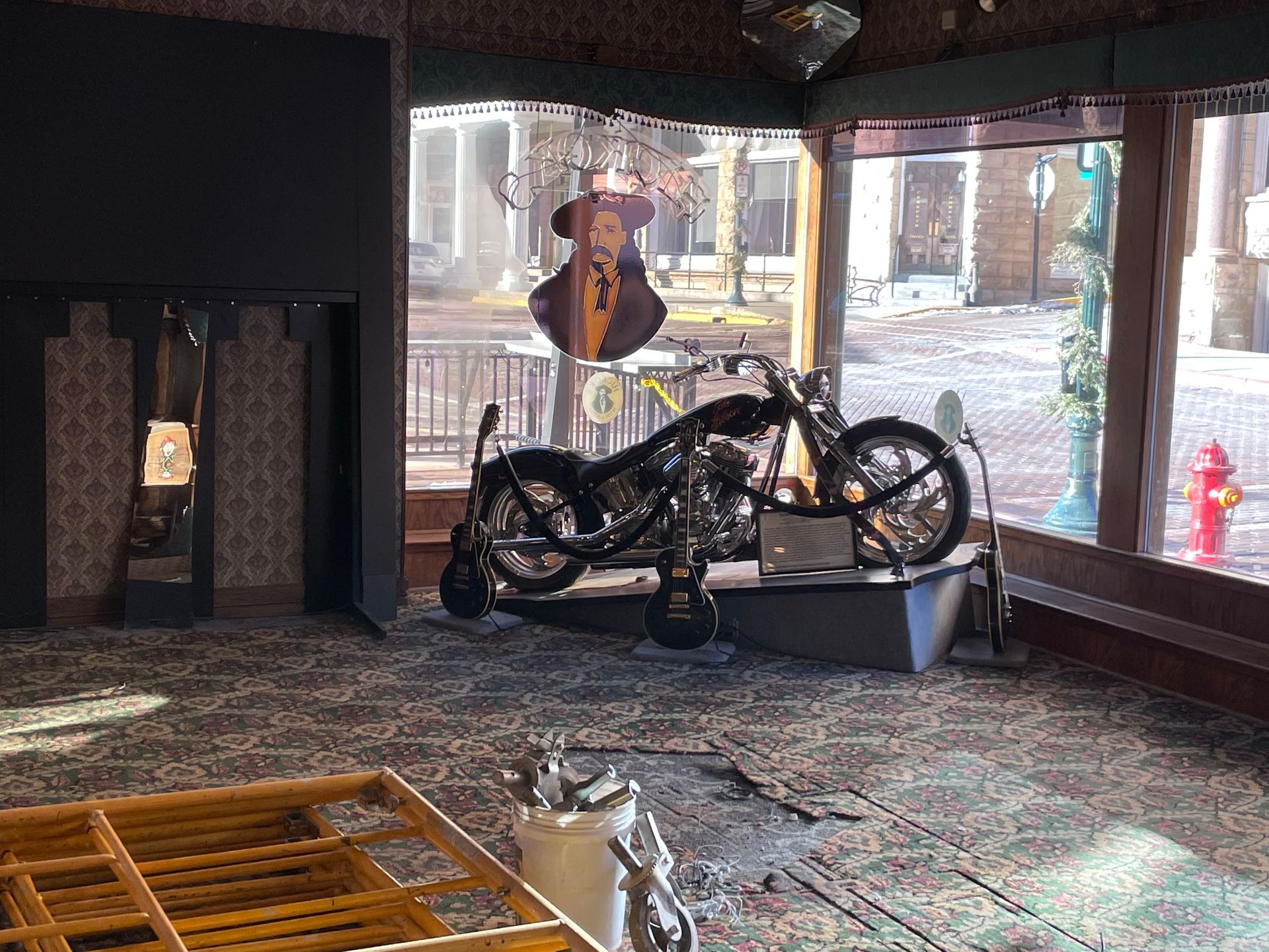 Motorcycle inside a building, near a window overlooking a street. Decorative Elvis Presley cutout.