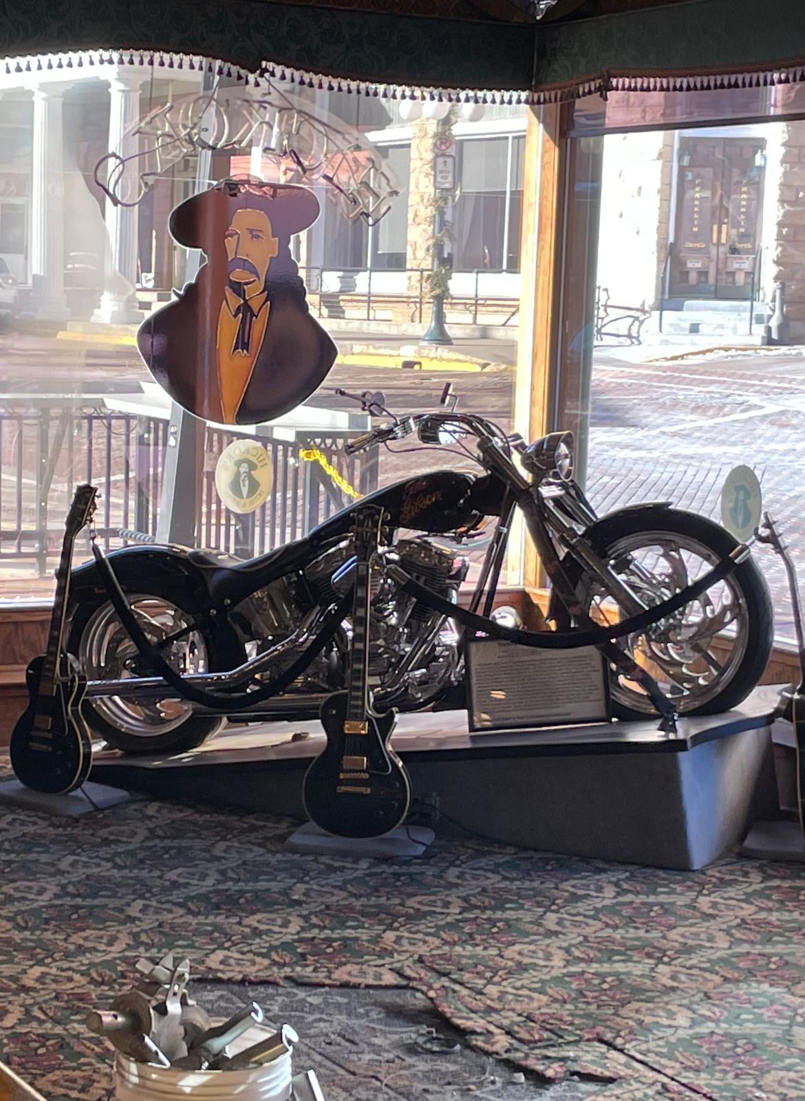 Motorcycle and guitars displayed in a window, with a cutout of a man in the background.