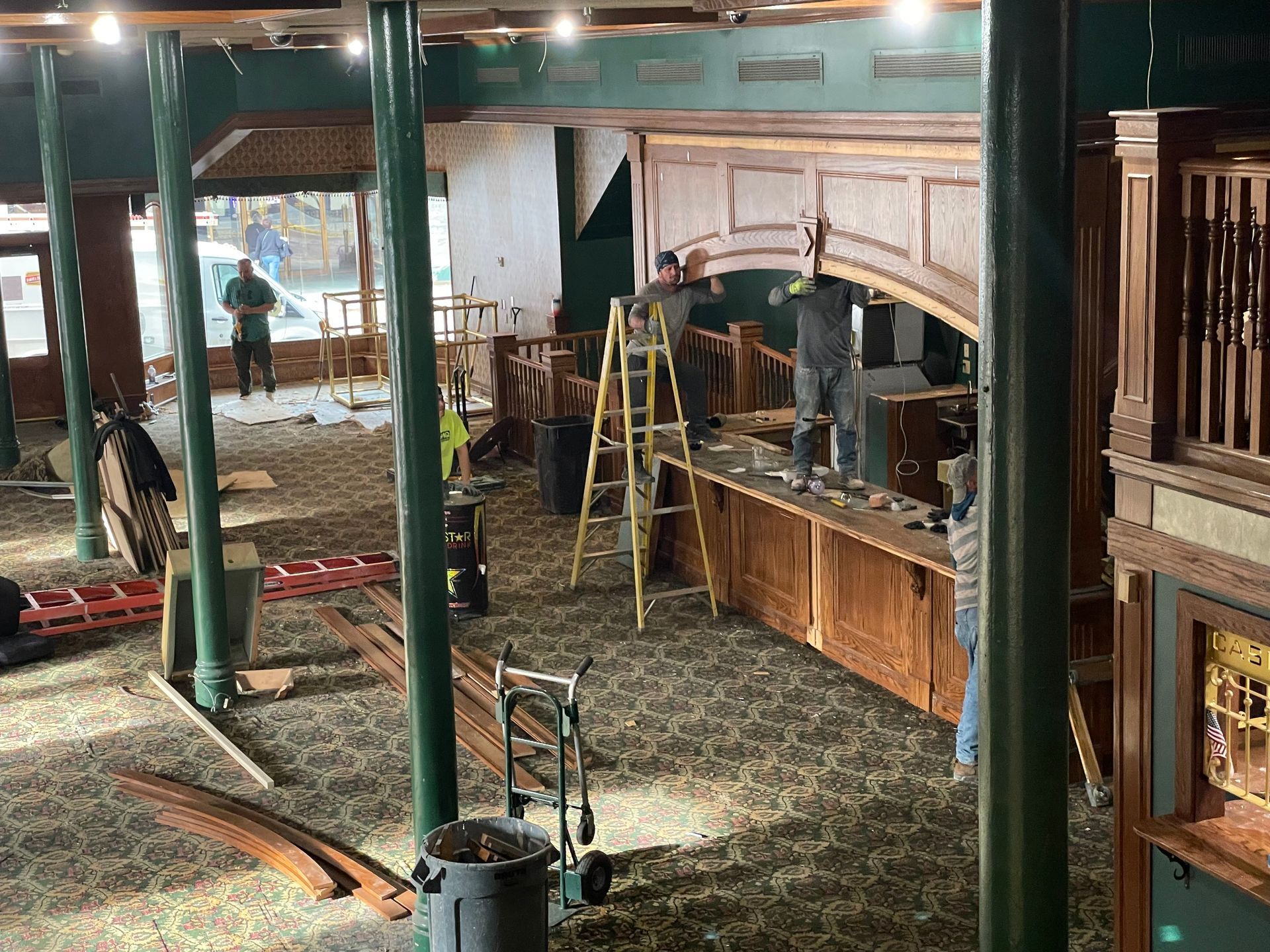Construction workers renovating a bar with green pillars and wooden detailing.