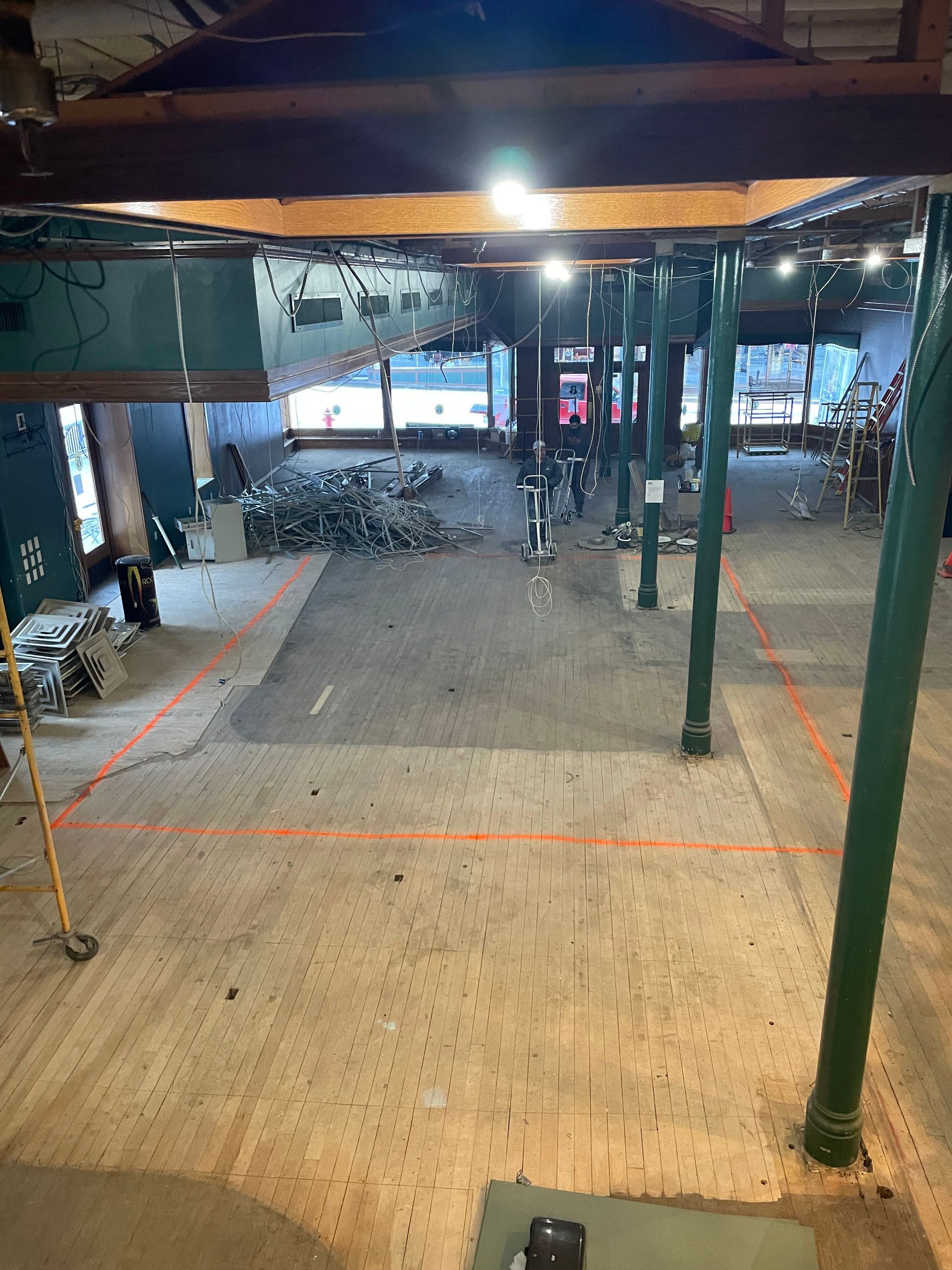 Interior view of a building under construction. Concrete floor with orange lines, green columns, exposed beams.