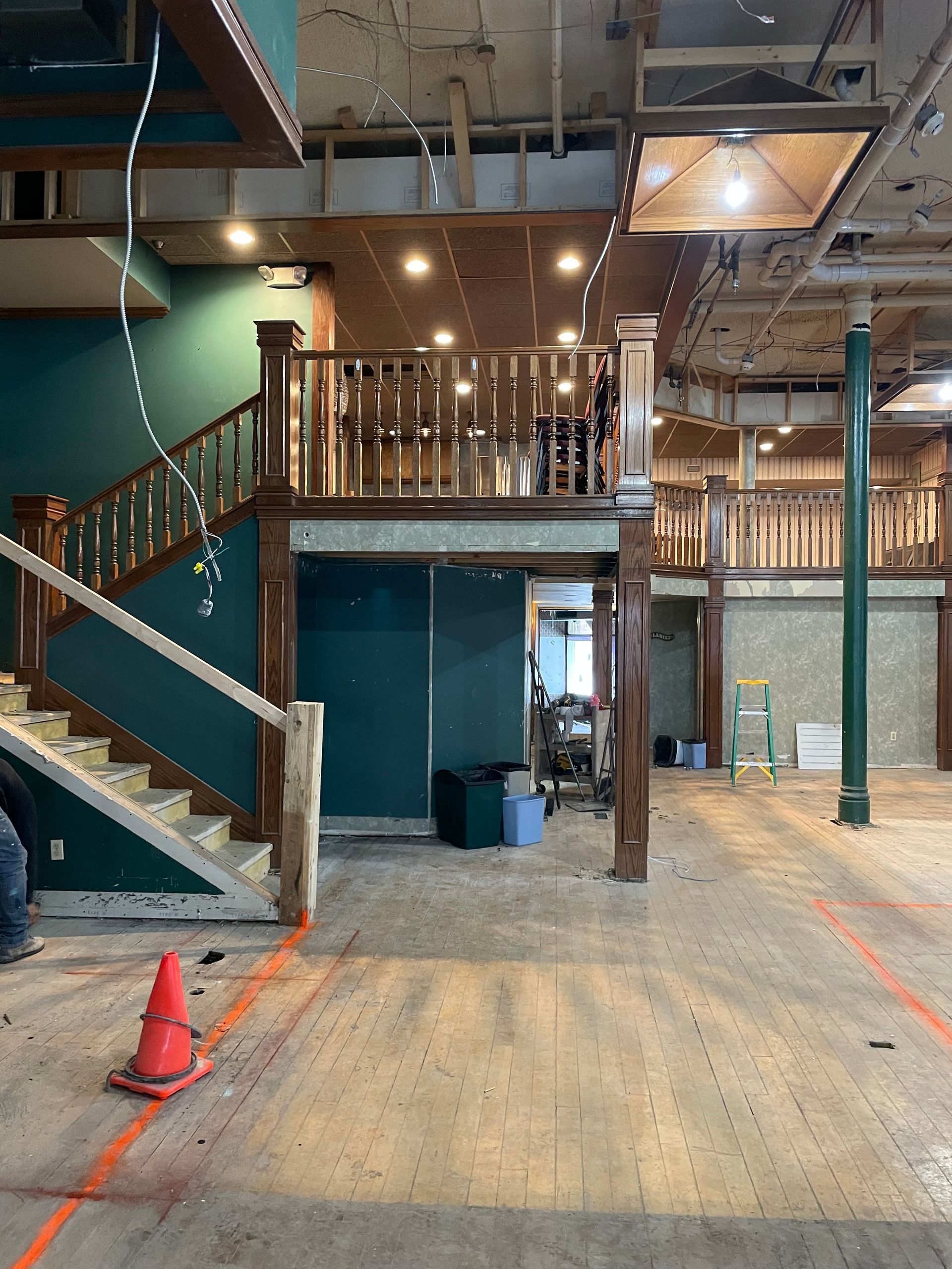Interior with a partially constructed second story and stairs, green and brown tones. Construction cone in foreground.