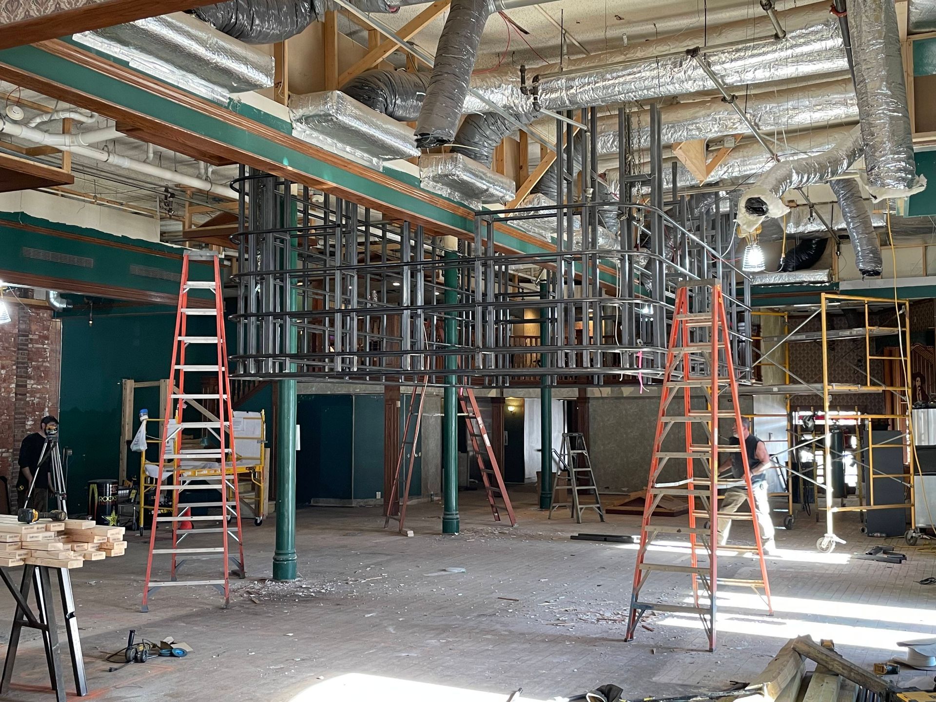 Interior construction site with metal framework, ladders, and exposed ceiling ductwork.