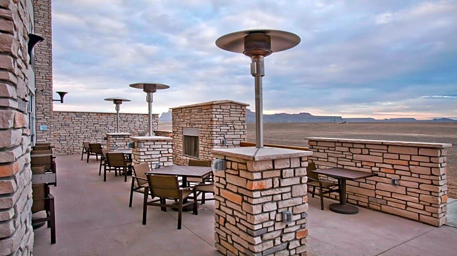 Outdoor patio with stone walls, tables, chairs, and heaters, overlooking a desert landscape.