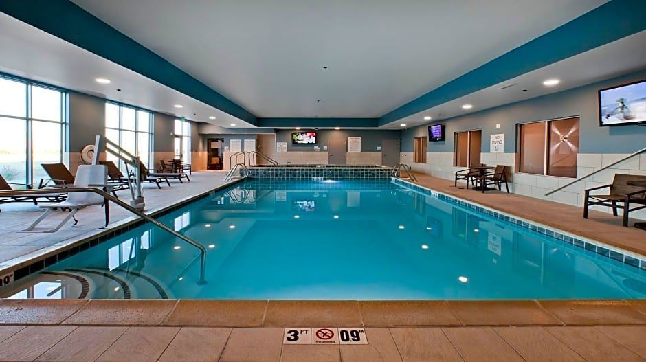 Indoor swimming pool with turquoise water, lounge chairs, and wall-mounted televisions.