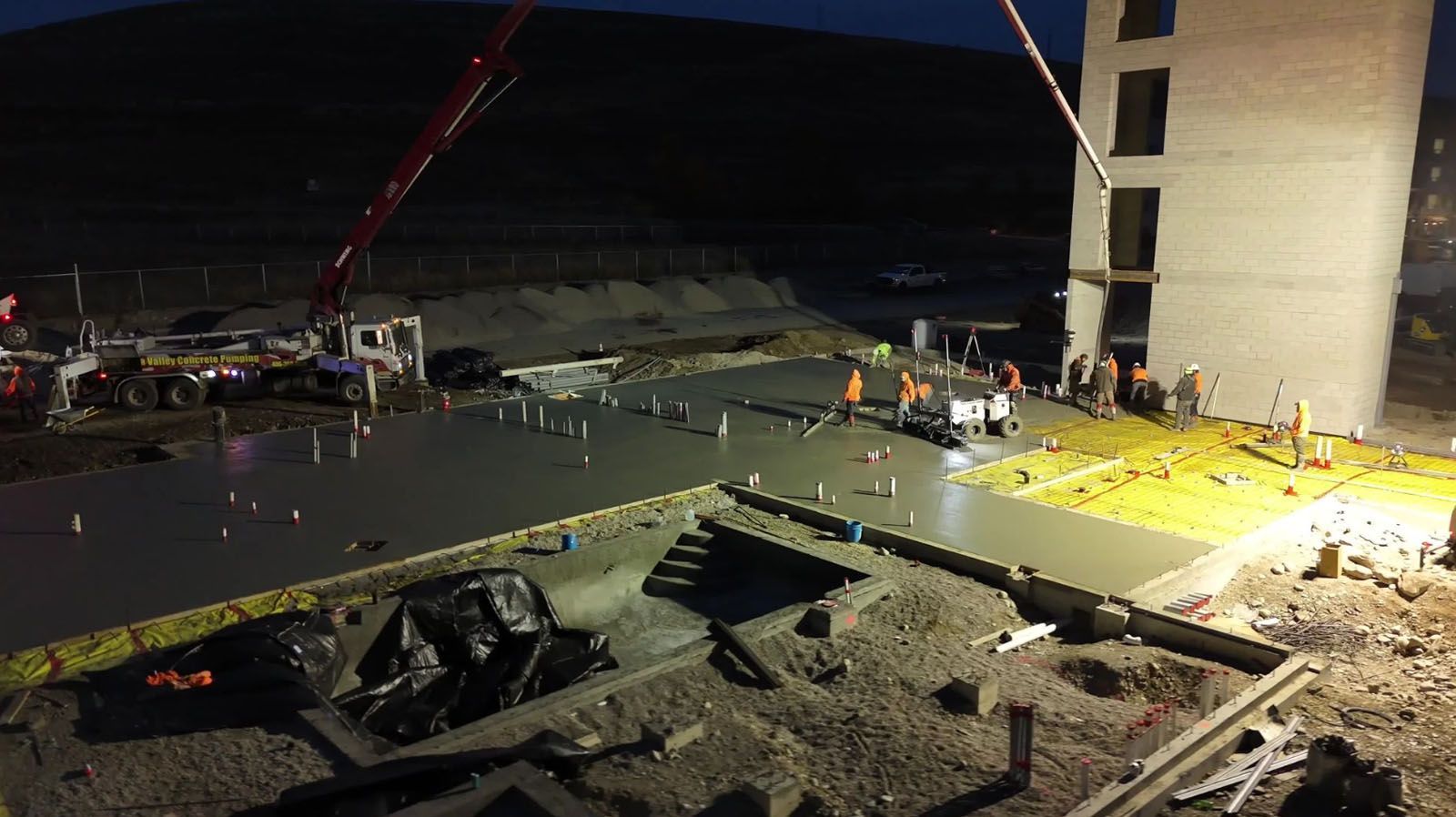 Construction site at night with concrete pouring. Workers, concrete pump, and building.
