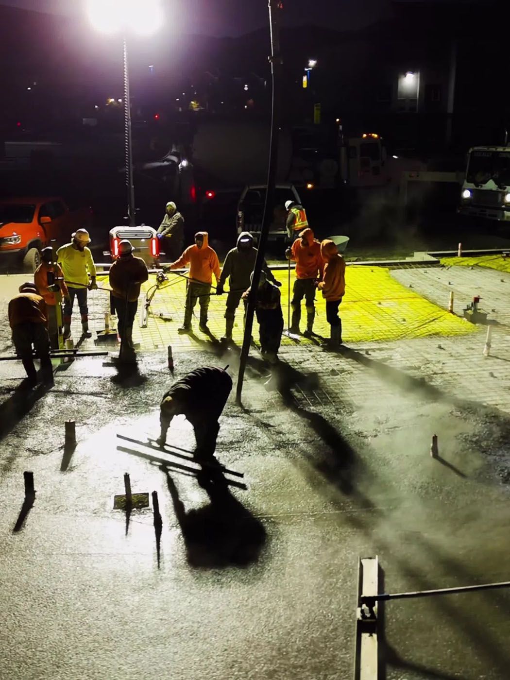 Construction workers pouring concrete at night, illuminated by bright lights.
