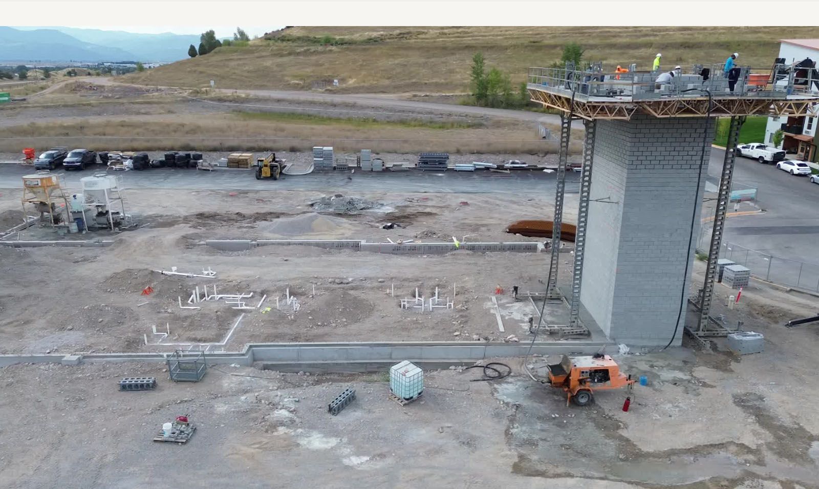 Construction site with a concrete column and scaffolding; workers on top.