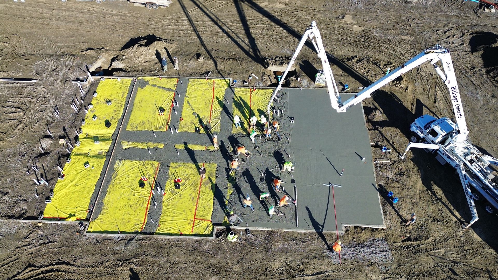 Aerial view: Construction workers pouring concrete foundation; a concrete pump truck, yellow insulation.