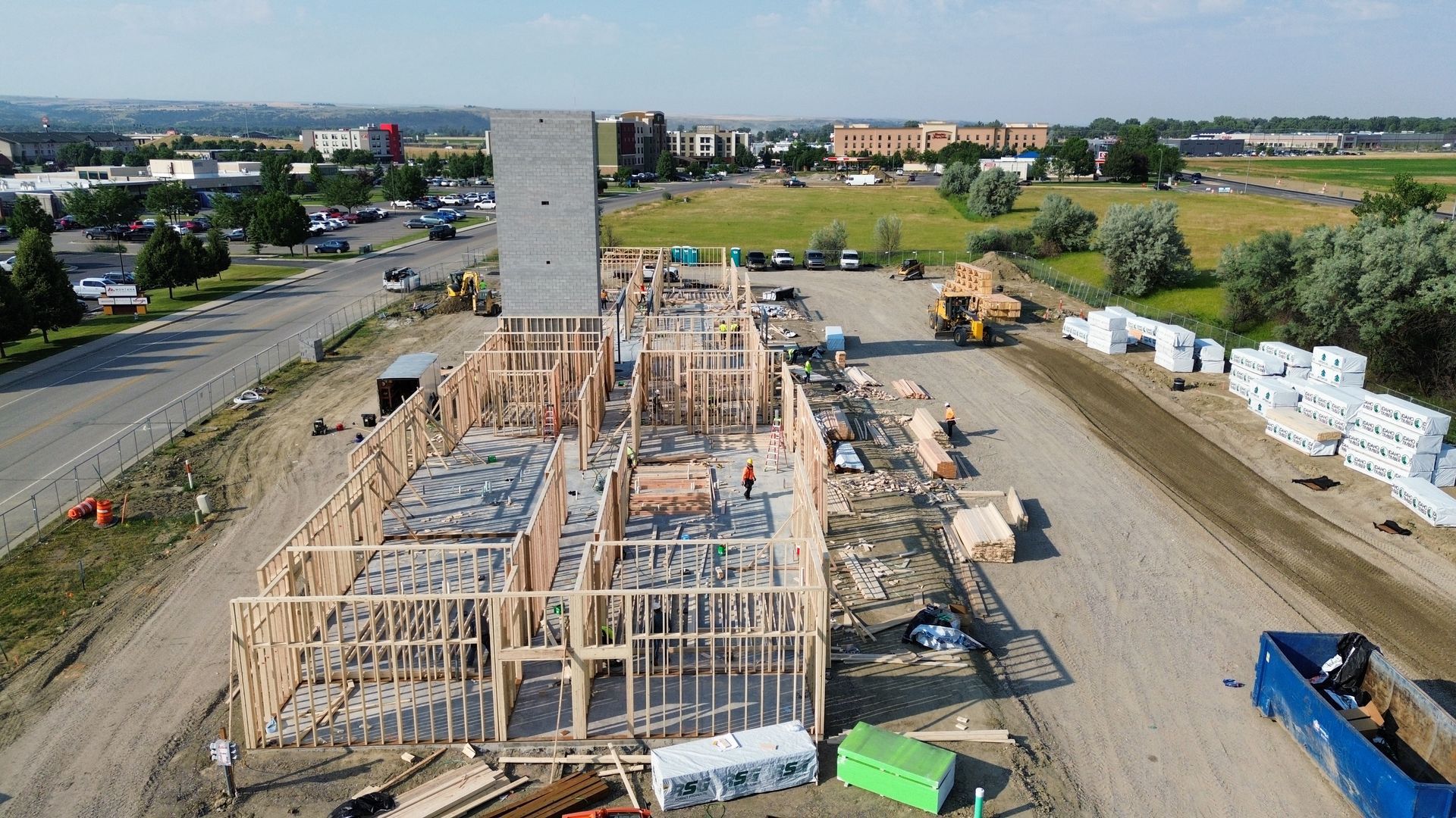 Construction site with wooden framework for a multi-story building. Lumber and heavy machinery visible.