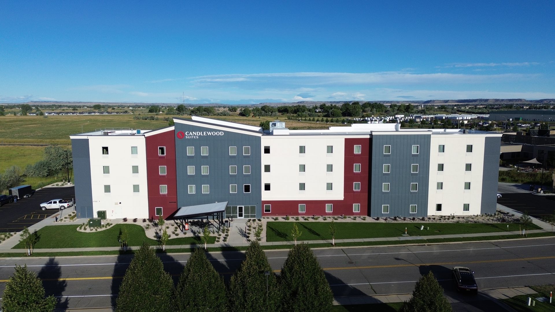 Hotel exterior with red, gray, and white facade. Landscaping and blue sky visible.