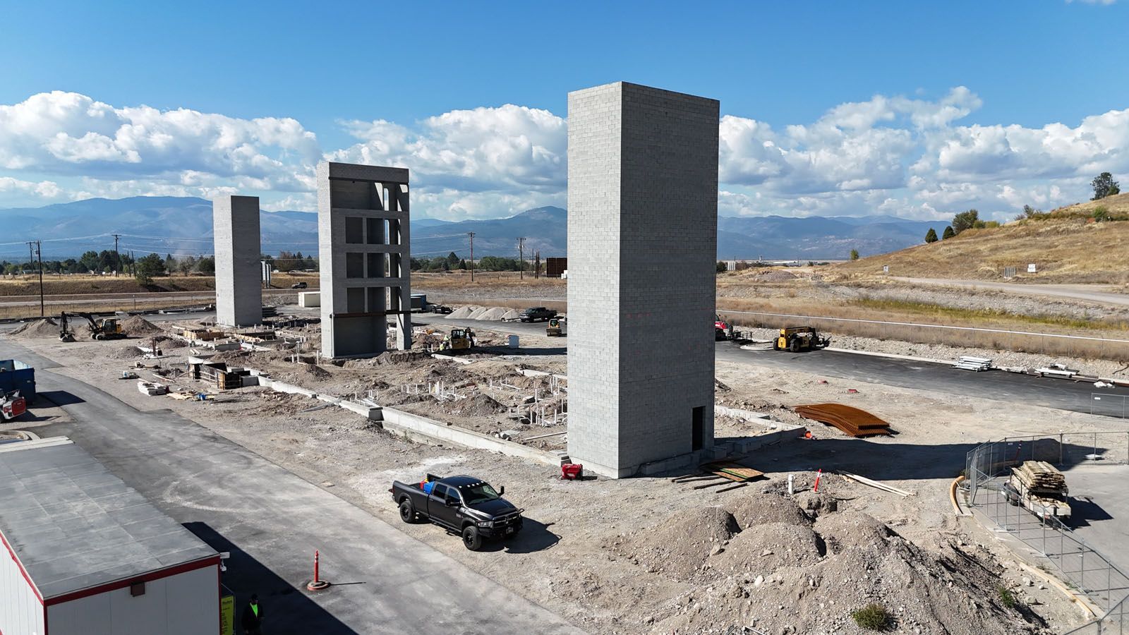 Construction site with several gray rectangular towers and a partially constructed building. Blue sky.