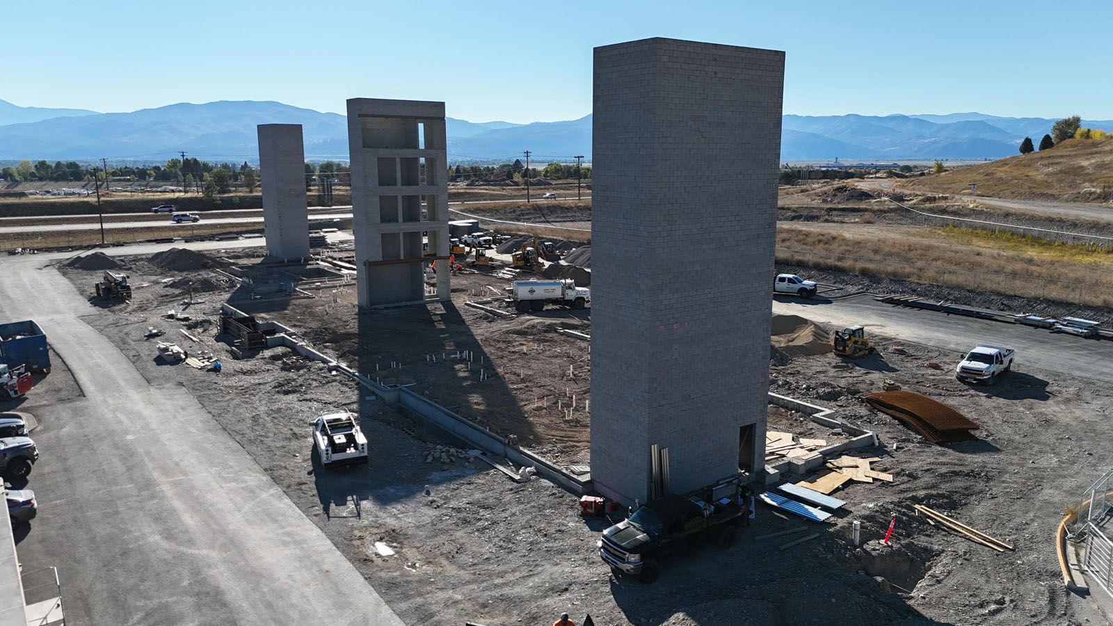 Construction site with three concrete pillars. Construction vehicles surround the pillars, with mountains in the background.