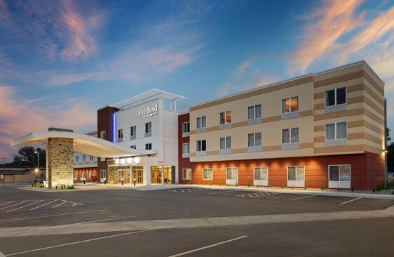 Hotel exterior with a covered entrance, parking lot, and evening sky.