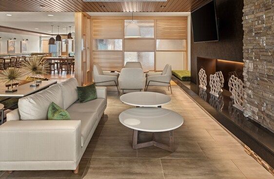 Modern hotel lounge with white sofa, light wood paneling, and stone fireplace.