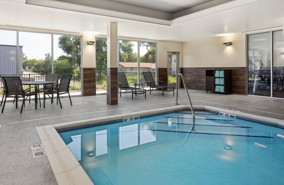 Indoor swimming pool with lounge chairs and tables beside large windows.