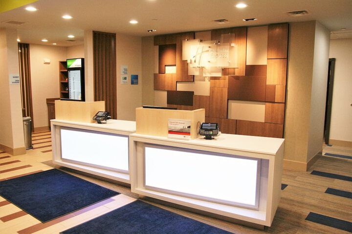 Hotel front desk with glowing white panels, blue carpet, and geometric wooden wall art.