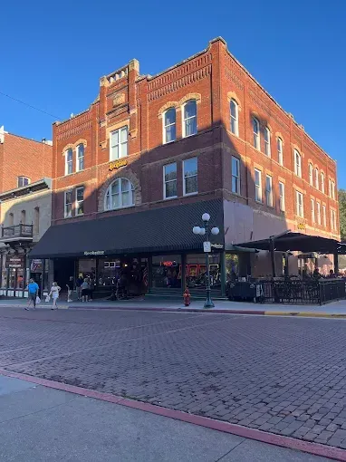 Brick building with a dark awning, street-level restaurant. People on the sidewalk and at outdoor seating.