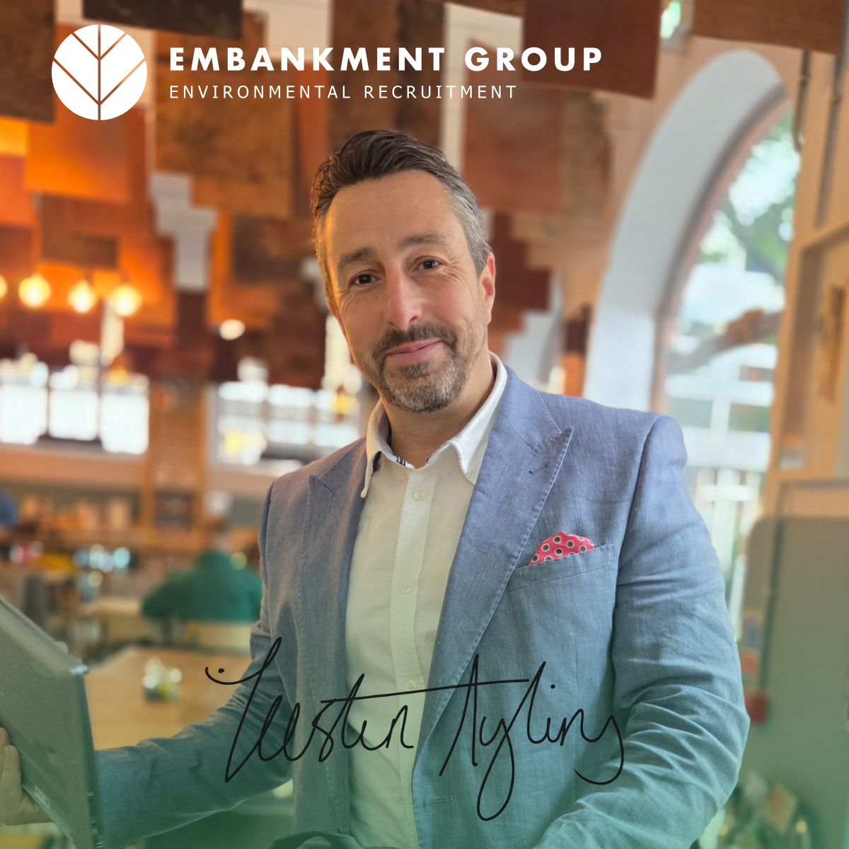 Ecology recruiter in a blazer smiles, standing indoors with a logo 