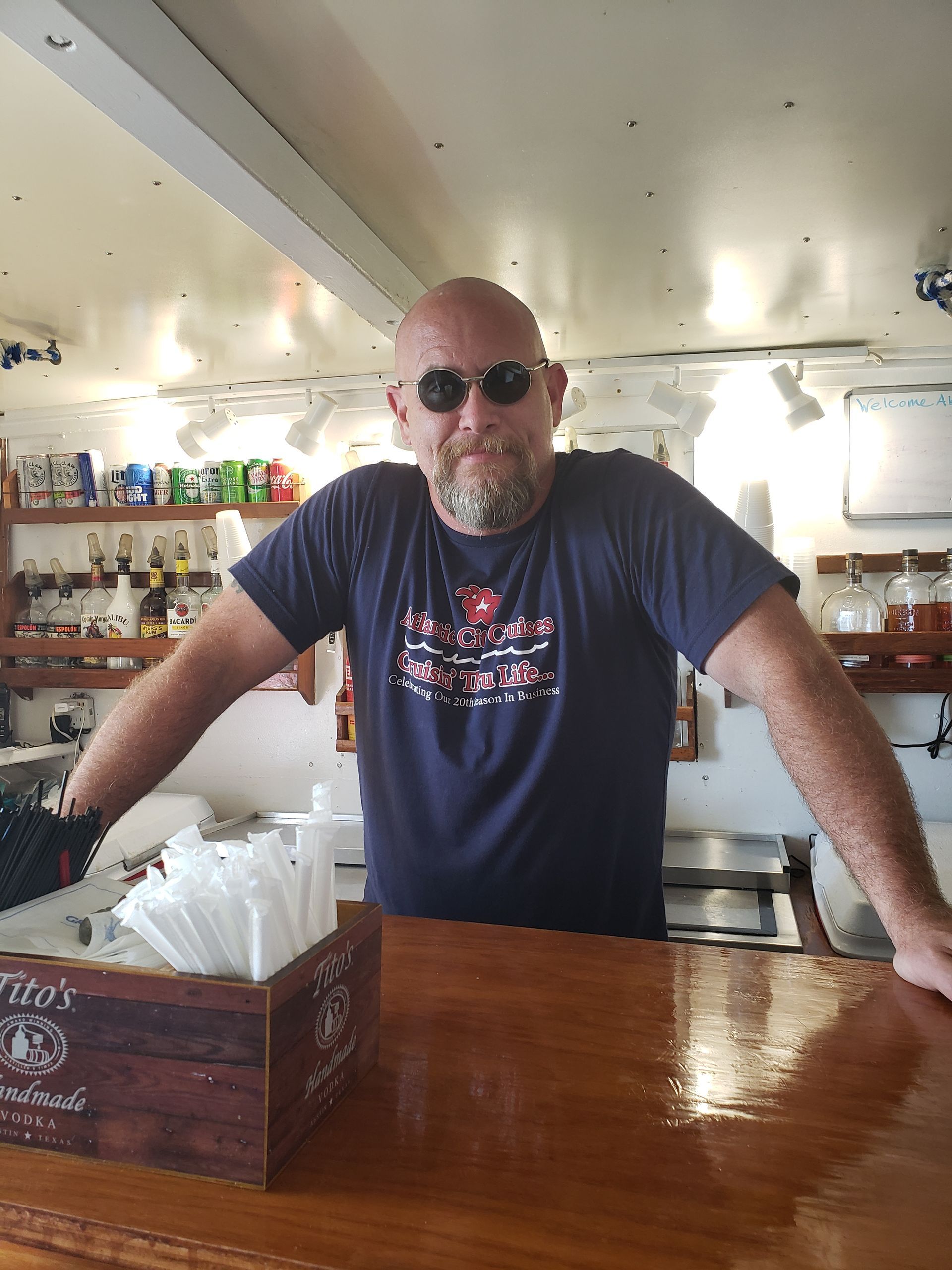 Man behind a wooden bar wearing sunglasses and a navy blue shirt.