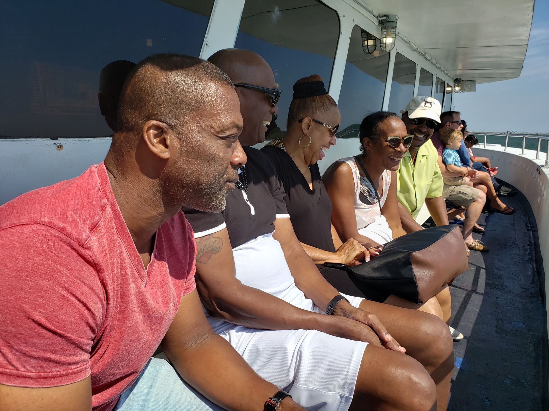 People on a boat looking at the view. One person laughs. Sunny day.