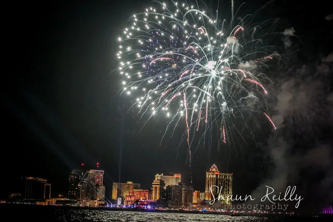 Fireworks exploding over a city skyline at night above a waterfront.