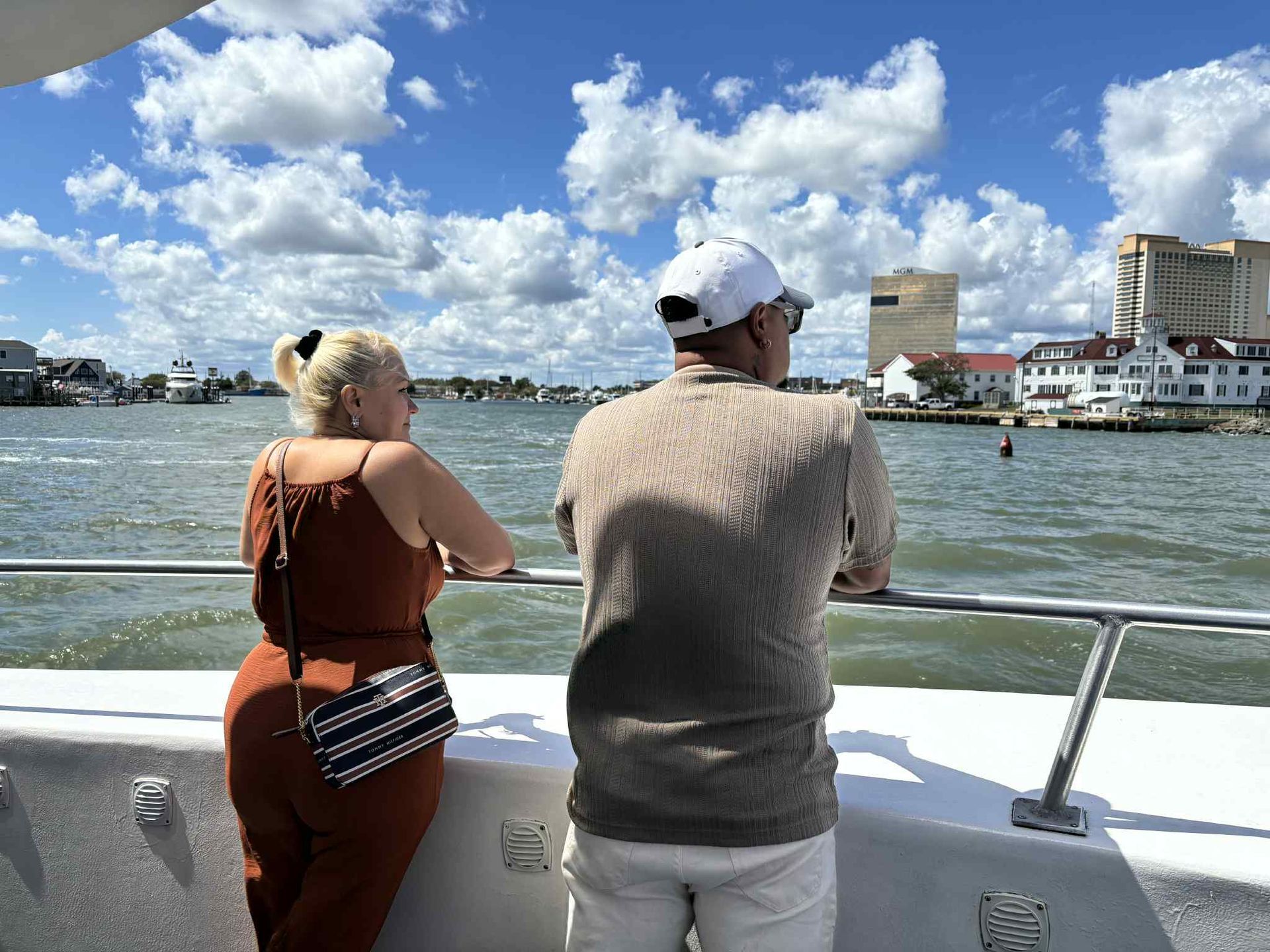 Couple on a boat looking at buildings on the water under a blue sky with clouds.