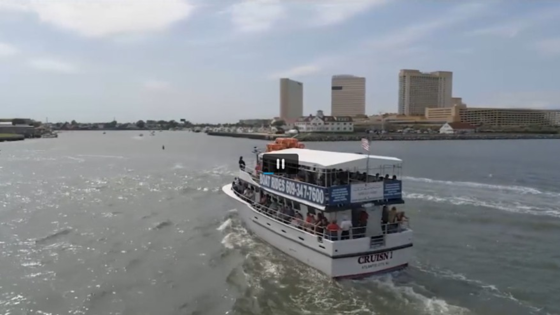 A white and blue tour boat sails on the water, with buildings in the background.