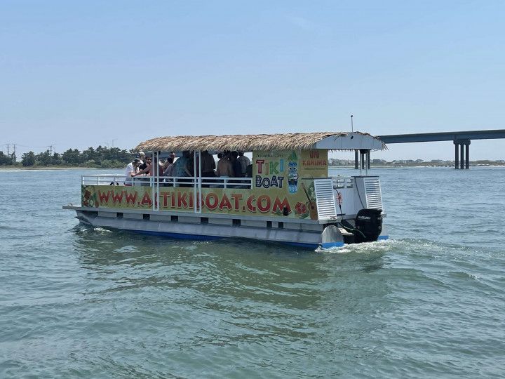 Tiki boat with passengers cruising on water, bridge in background.