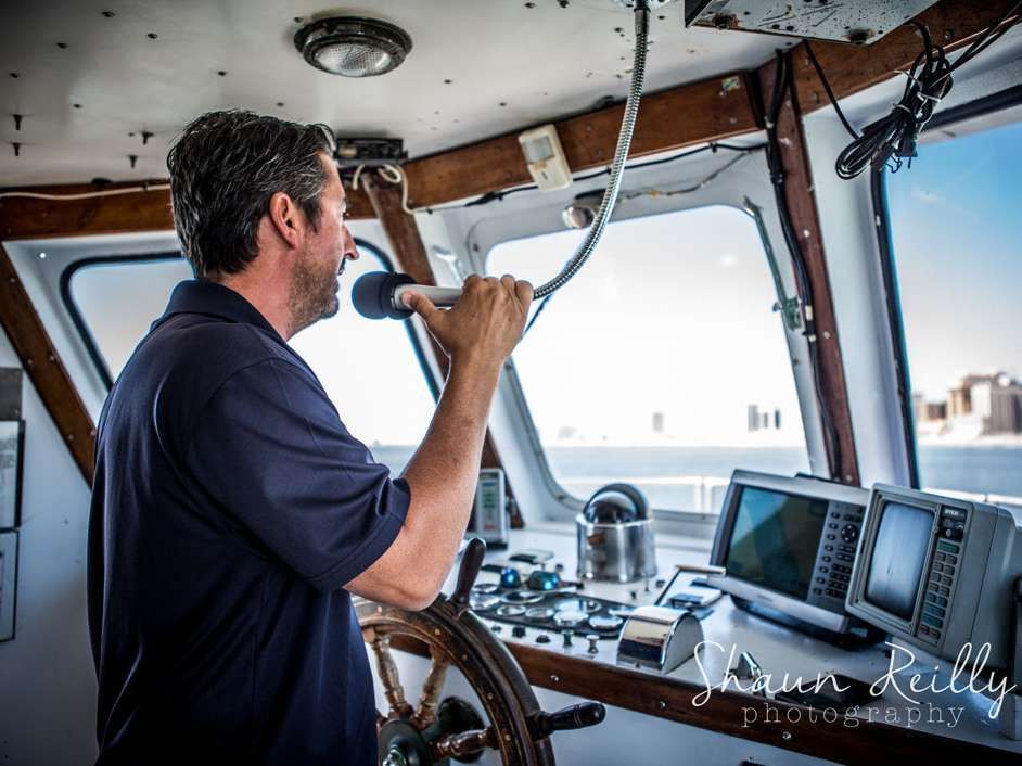Man speaking into a microphone on a boat's bridge, looking at sea.