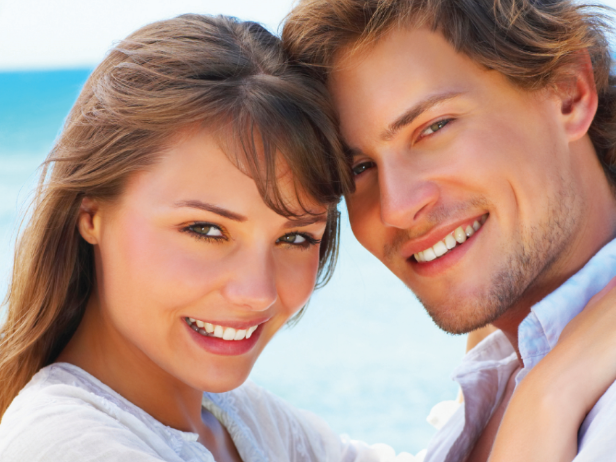 Smiling couple embracing near a body of water, sunny day.