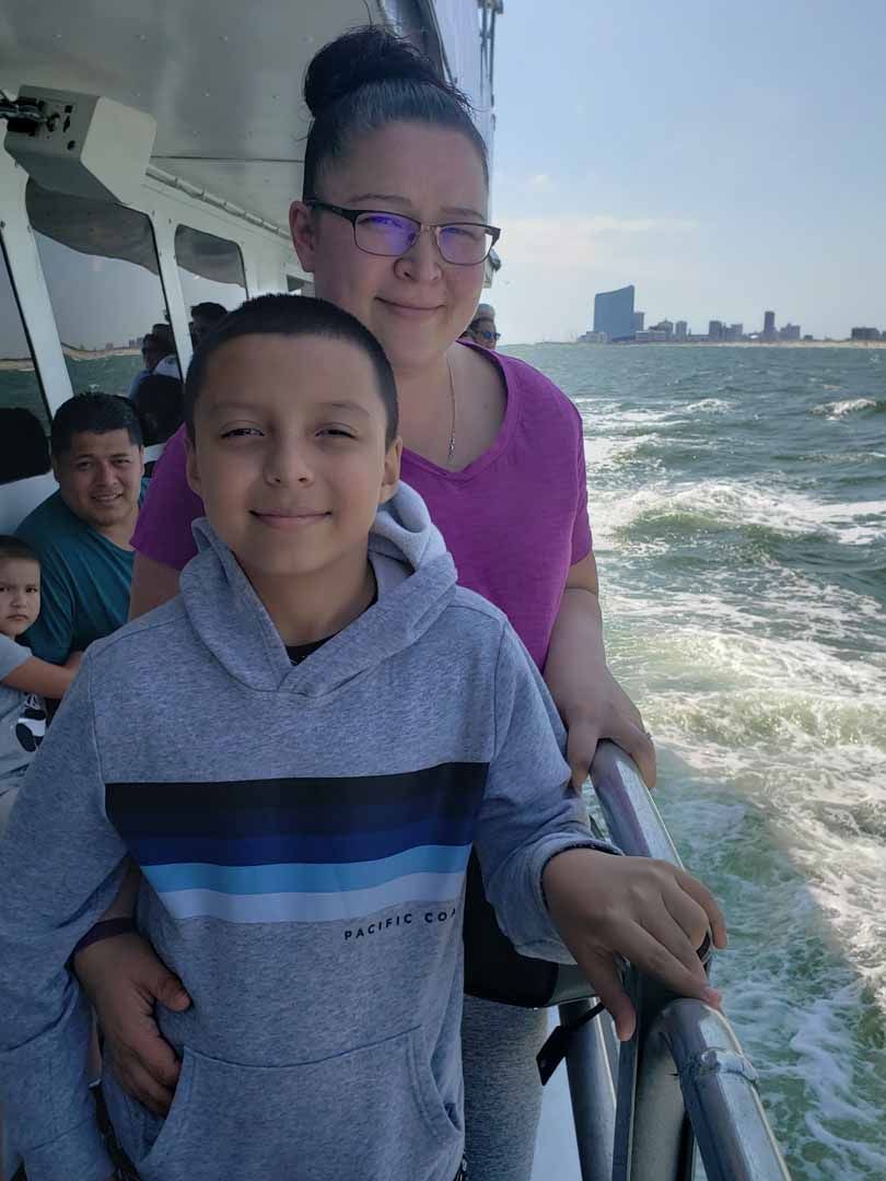 Boy and woman on a boat; water and city skyline in the background. They are smiling.
