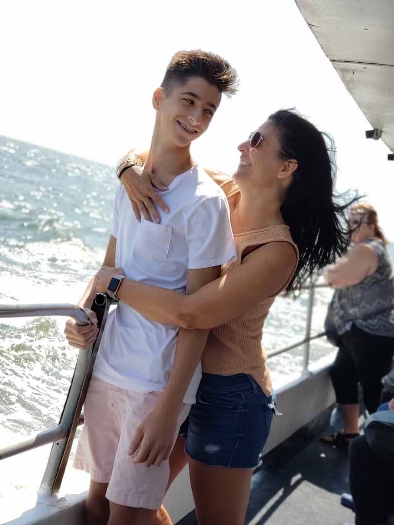 Woman hugging person on a boat, smiling, with ocean in the background.