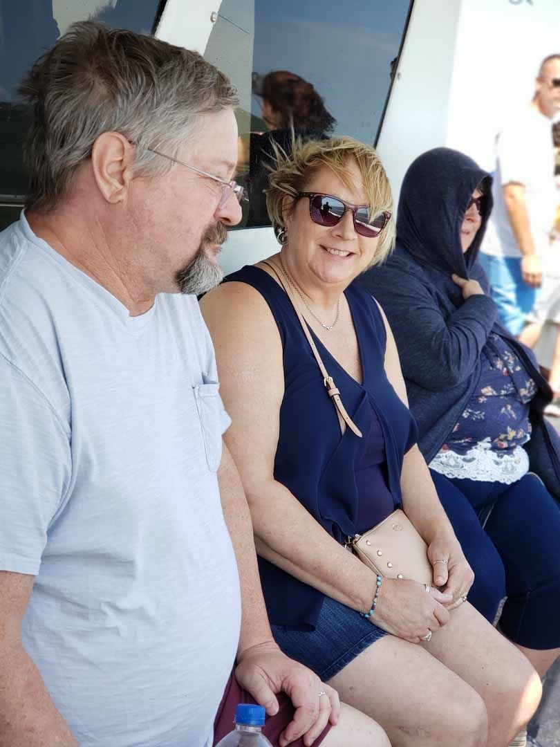 Three people sitting outdoors. One with glasses and a beard, one with sunglasses smiling, one in a hood.