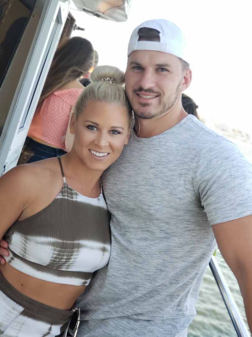Woman with blonde bun and man in a white cap, smile close together on a boat.