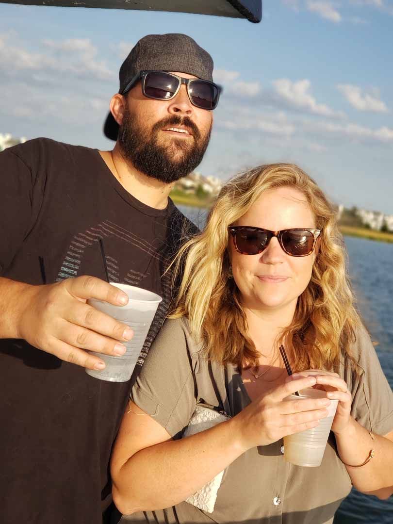 Man and woman on a boat, wearing sunglasses and holding cups.