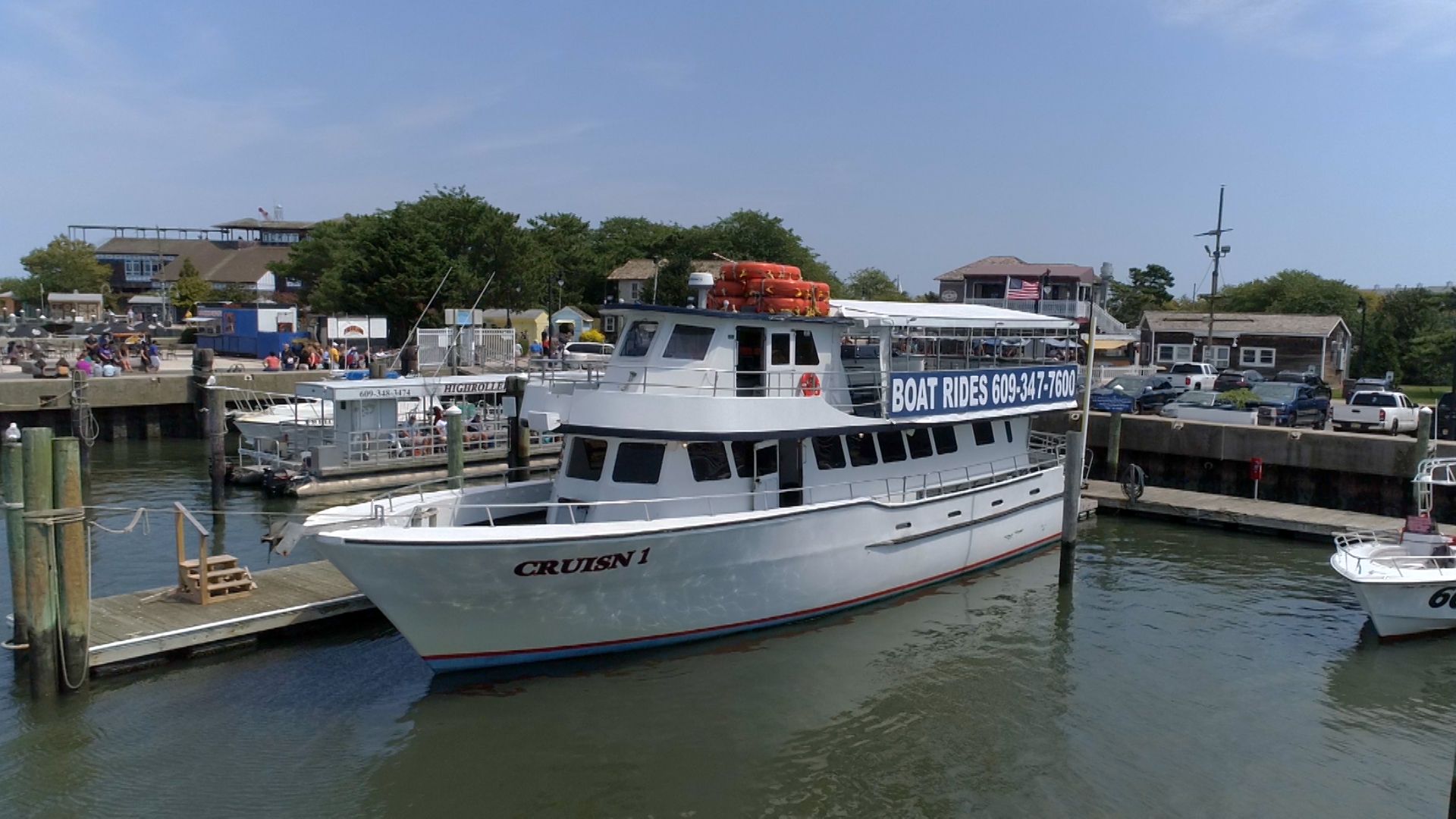 White passenger boat docked in harbor on a sunny day. Buildings and people visible on the pier.