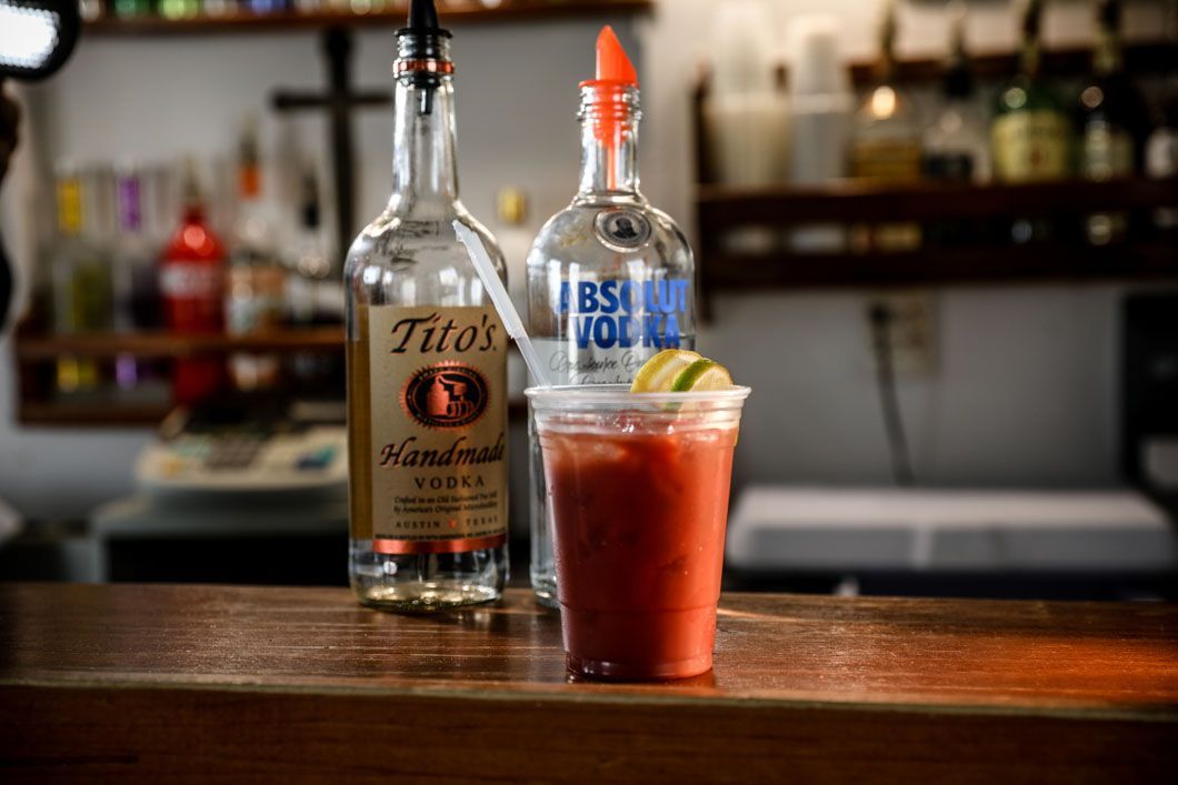 Bloody Mary cocktail in a plastic cup with two vodka bottles on a bar.