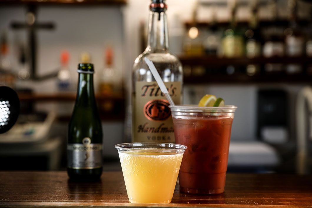 Cocktails on bar: bottle of vodka, champagne, two drinks in plastic cups; one orange, one red.
