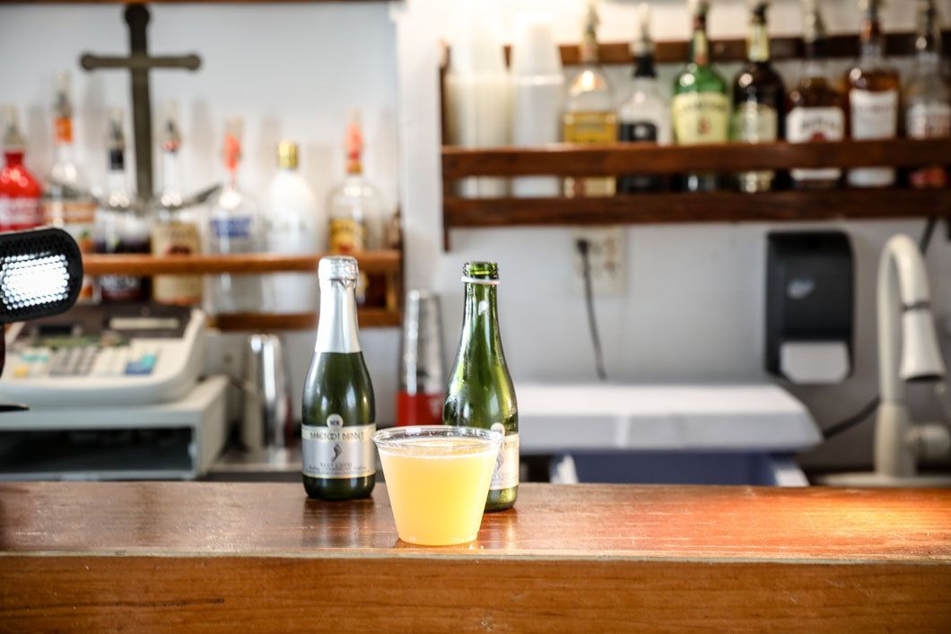 A bar with a drink in a plastic cup and bottles, shelves with liquor in the background.