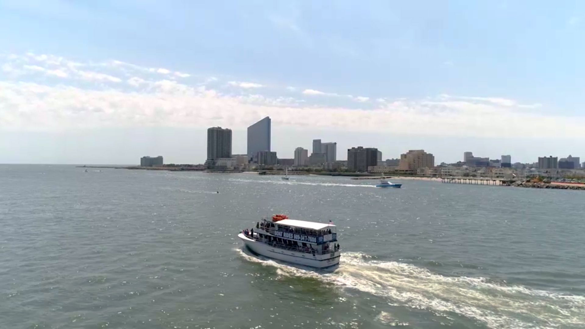 Boat sailing towards a city skyline on a sunny day.