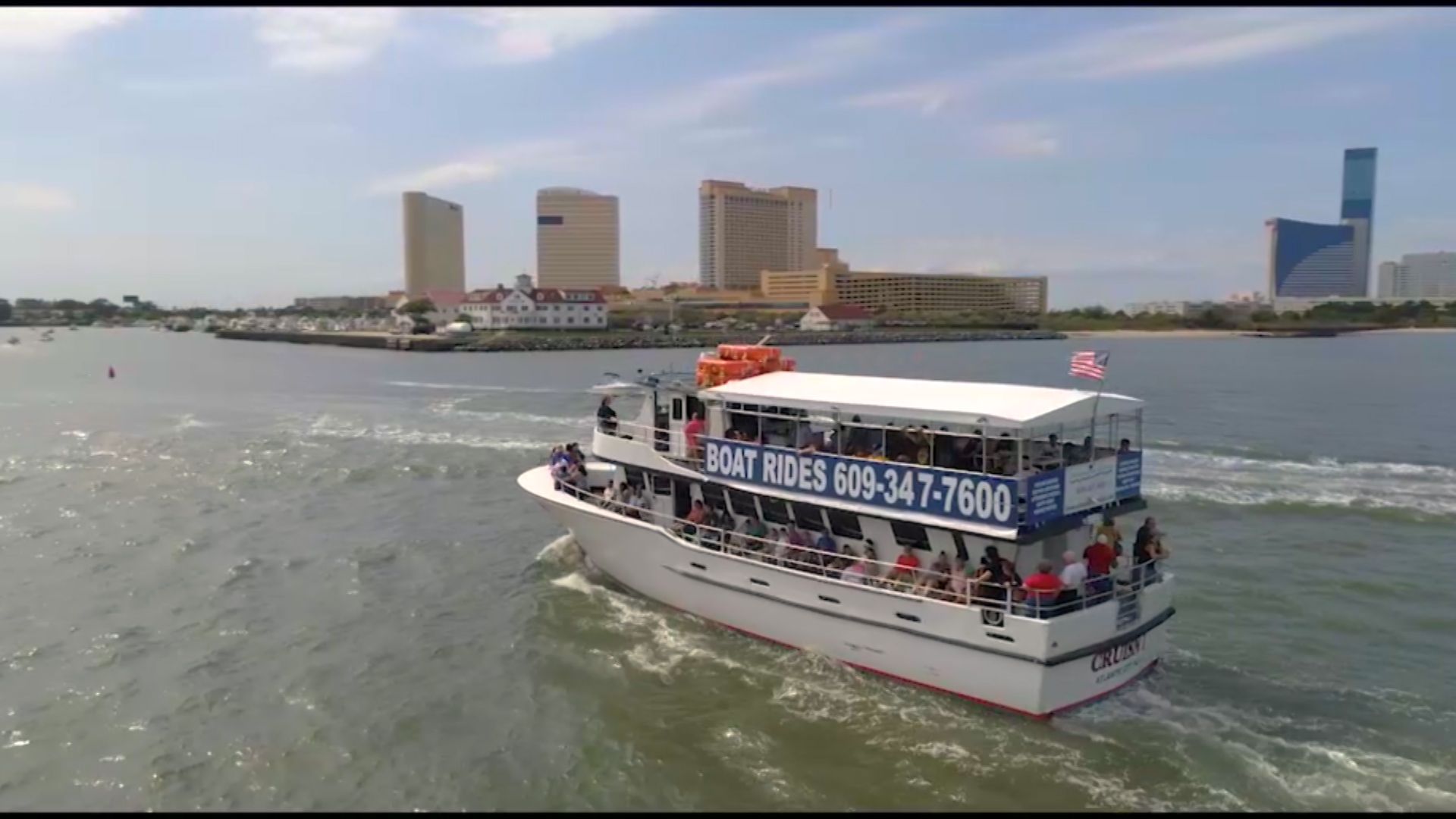 Boat on water, cruising past buildings. Blue sky. 