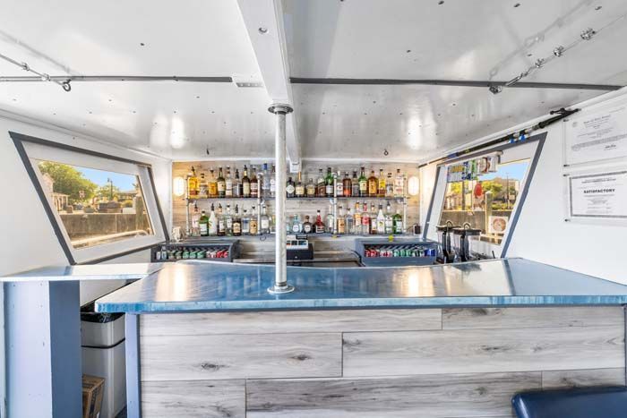 Bar inside a boat with bottles, glasses, and bar counter. Two open windows show outside view.