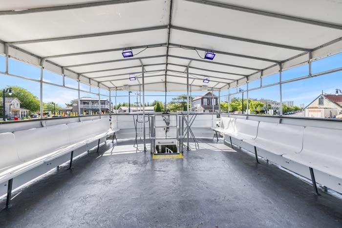Interior of a boat with white benches, gray floor, metal frame, and a white canvas roof.