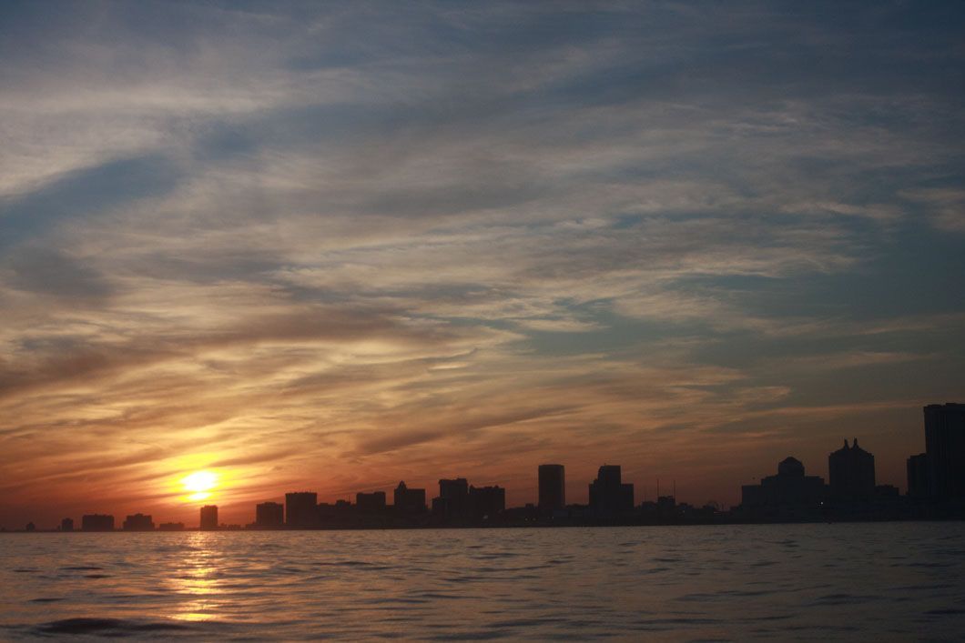 Sunset over water with city skyline silhouetted. Orange and yellow sky with reflective light on the water.